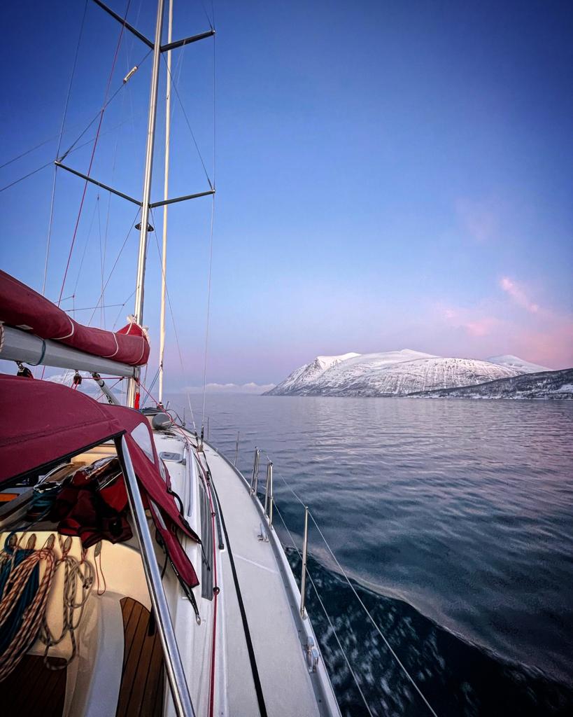 Sailing yacht under way at dusk with snow-covered mountains astern