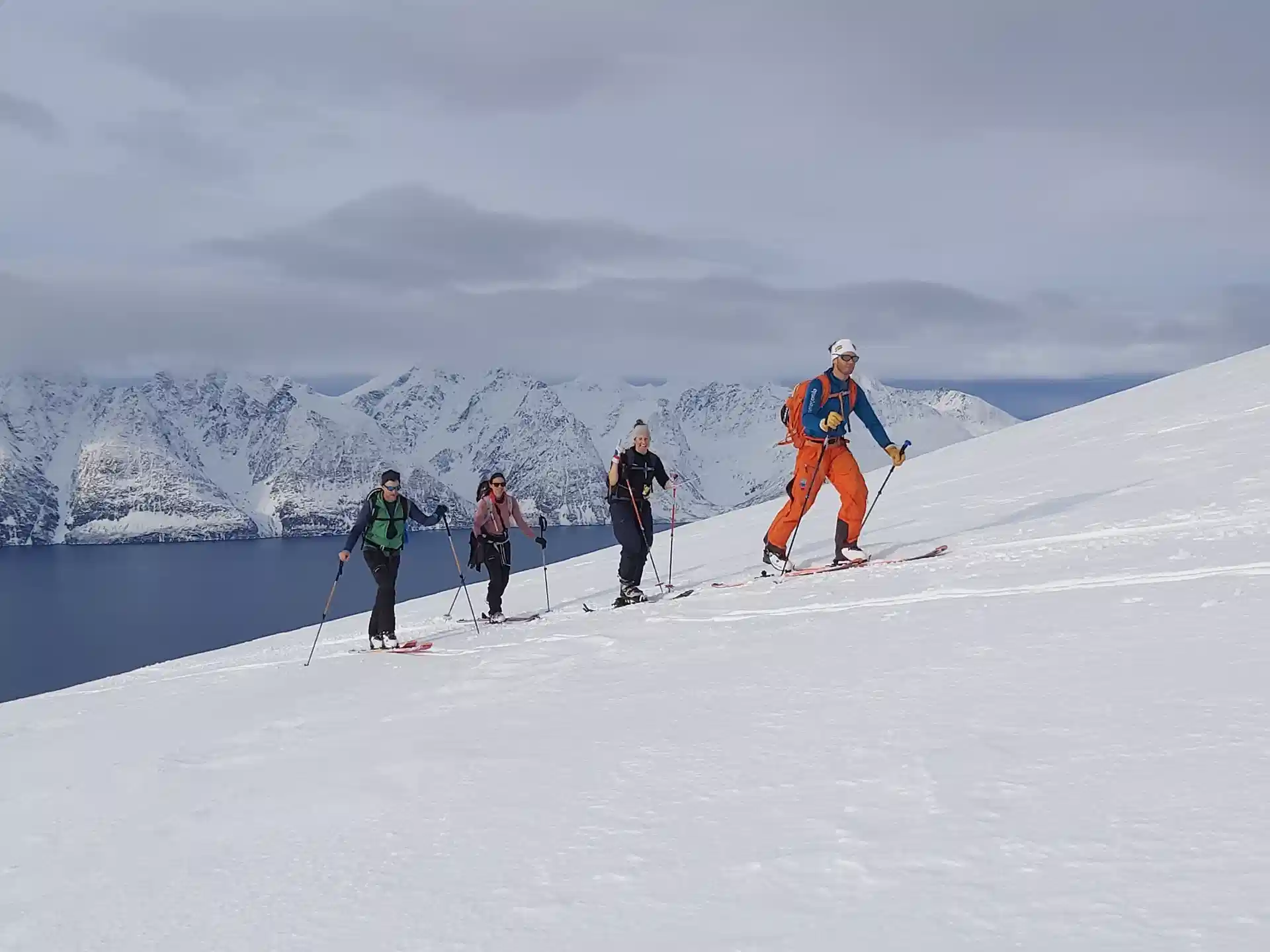 Ski tourers climbing a snow slope above the Lyngenfjord with a sailing yacht anchored below